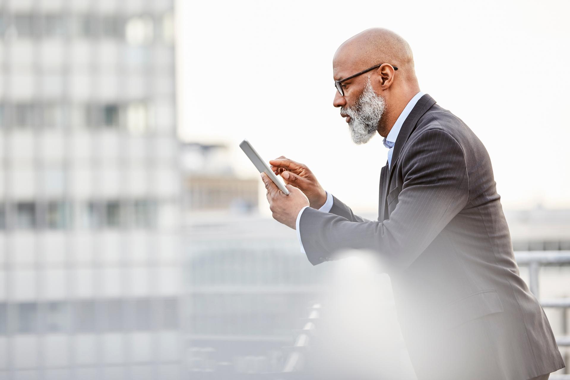 A businessman leans against a railing and looks at his smartphone