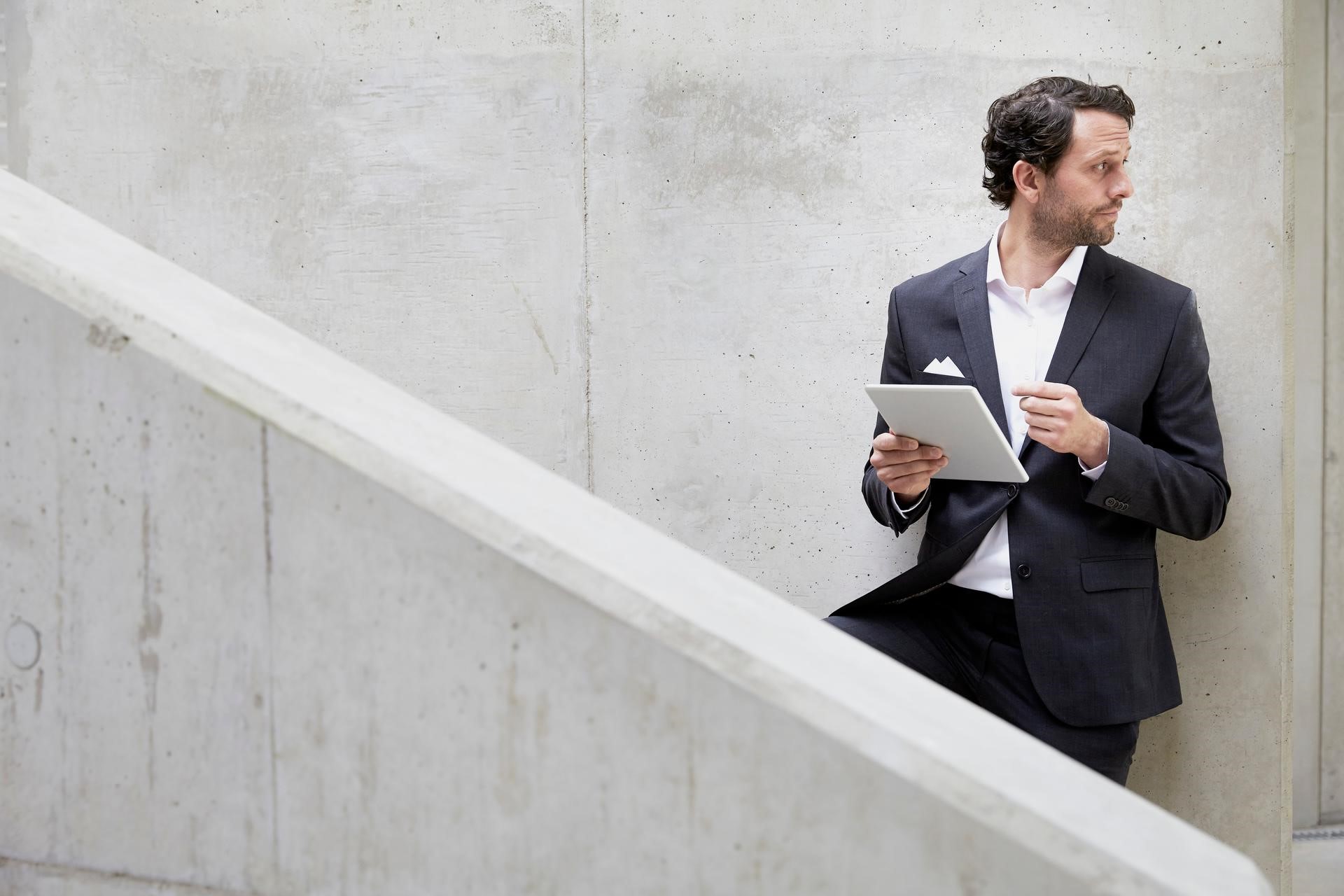 A man is standing on stairs and working on his tablet.
