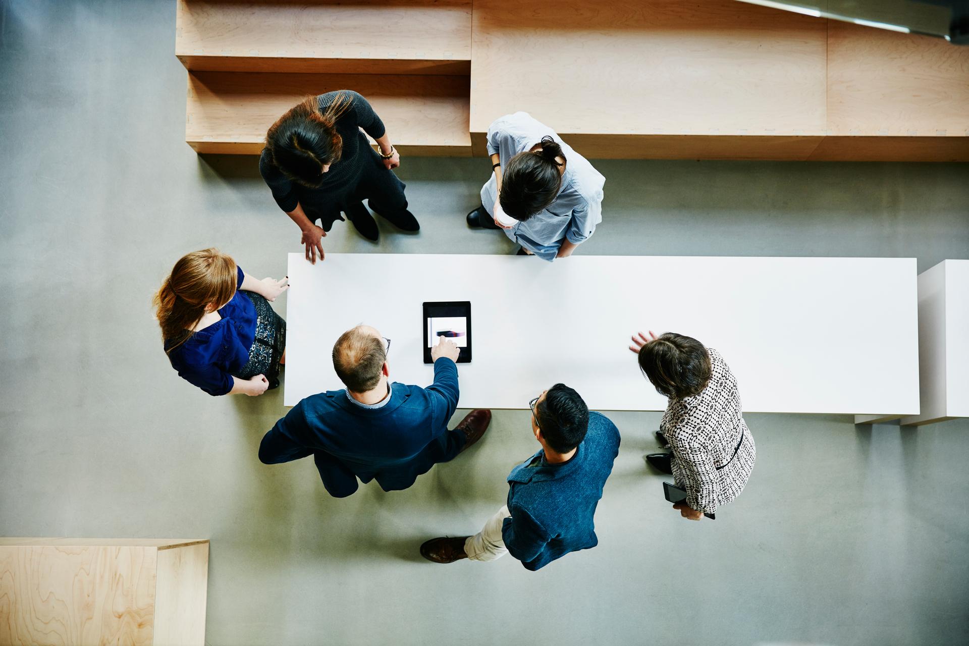Several employees stand around a table and look at a tablet